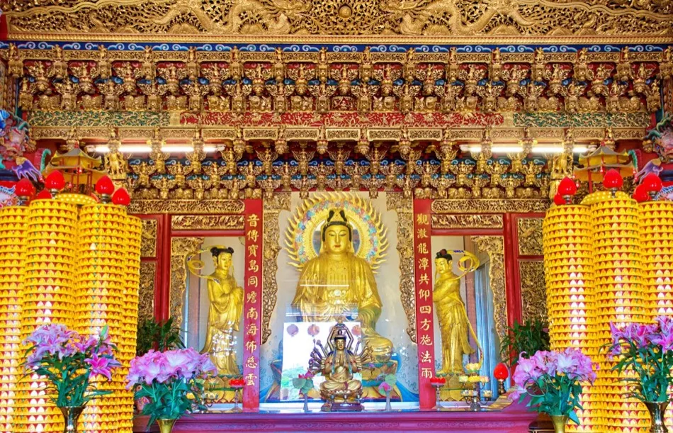 An ornate Chinese Mahāyāna altar with a golden Guanyin Bodhisattva, offering-lamp towers, and lotus flowers